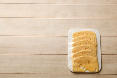 Photo of Pack of sliced cheese on wooden table, top view. Space for text