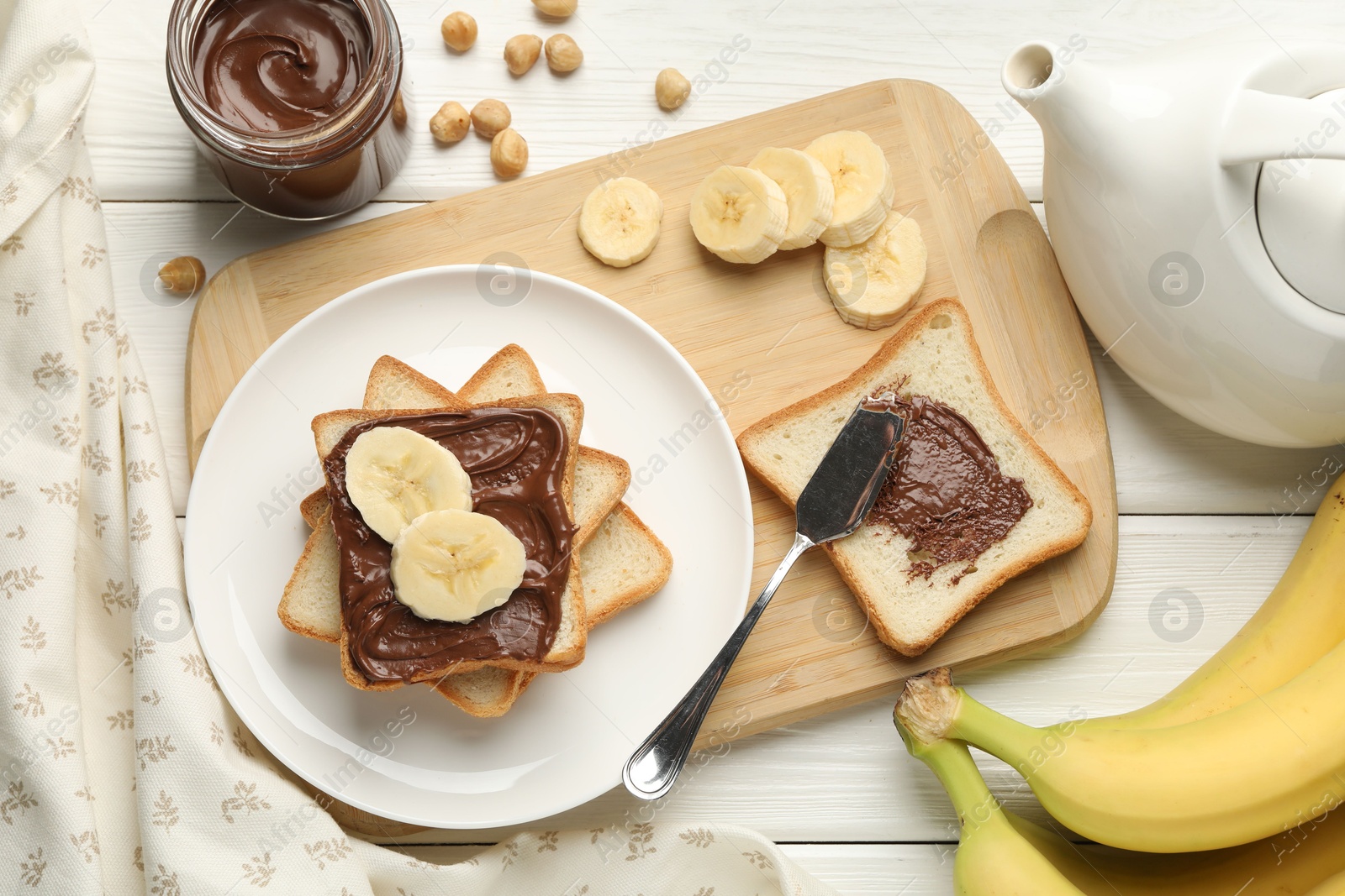 Photo of Sandwiches with chocolate butter, bananas and hazelnuts on white wooden table, flat lay