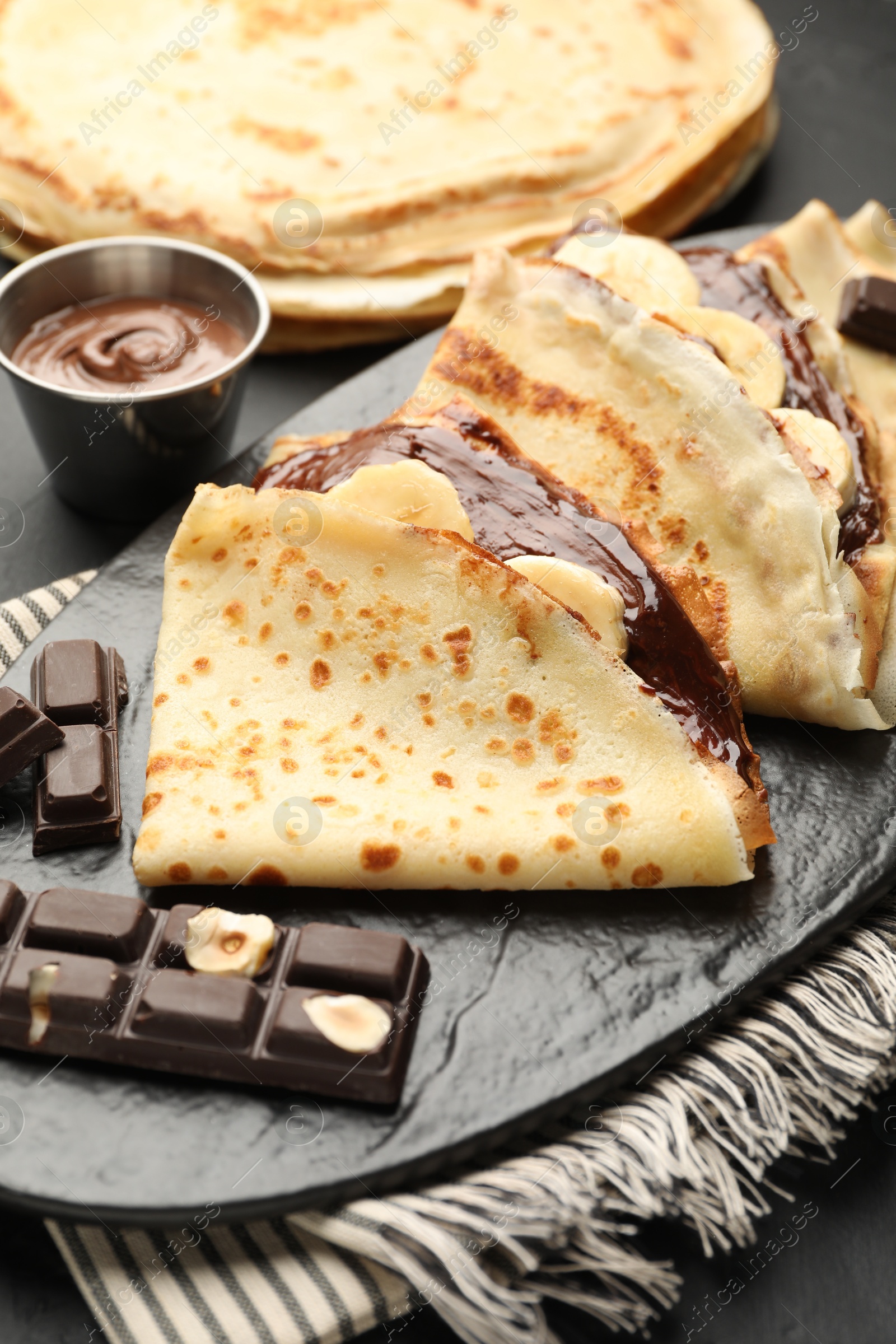 Photo of Tasty crepes with chocolate butter and banana on table, closeup