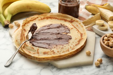 Photo of Tasty crepes with chocolate butter, bananas and hazelnuts on white marble table, closeup