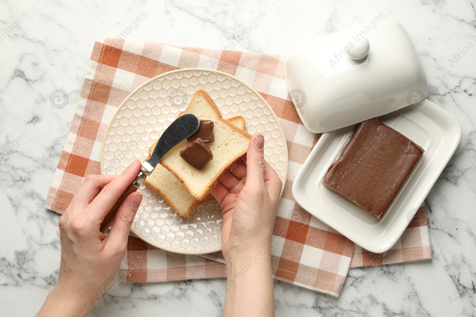 Photo of Woman spreading tasty chocolate butter onto bread at white marble table, top view