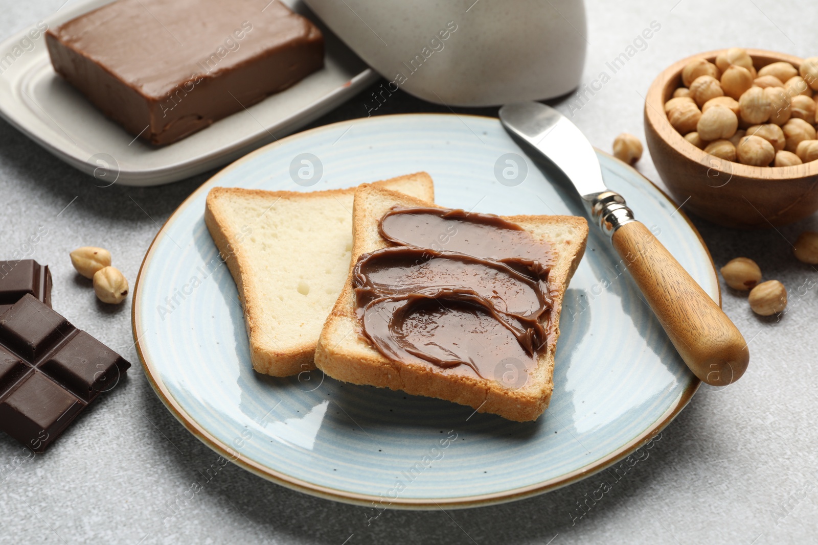 Photo of Sandwiches with chocolate butter, hazelnuts and knife on grey table, closeup