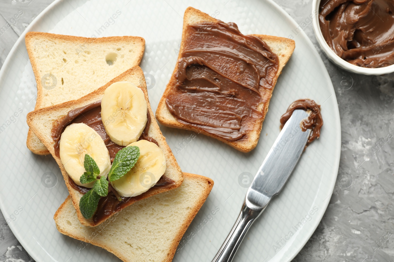 Photo of Sandwiches with chocolate butter, banana, mint and knife on grey table, top view