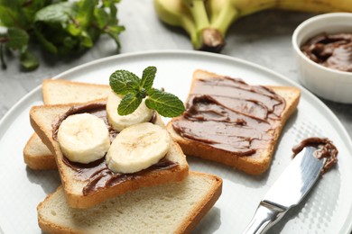 Photo of Sandwiches with chocolate butter, bananas, mint and knife on table, closeup