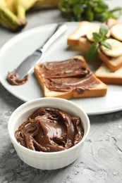 Photo of Tasty chocolate butter in bowl, sandwiches, bananas, mint and knife on grey table, closeup