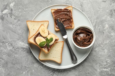 Photo of Sandwiches with chocolate butter, banana, mint and knife on grey table, top view