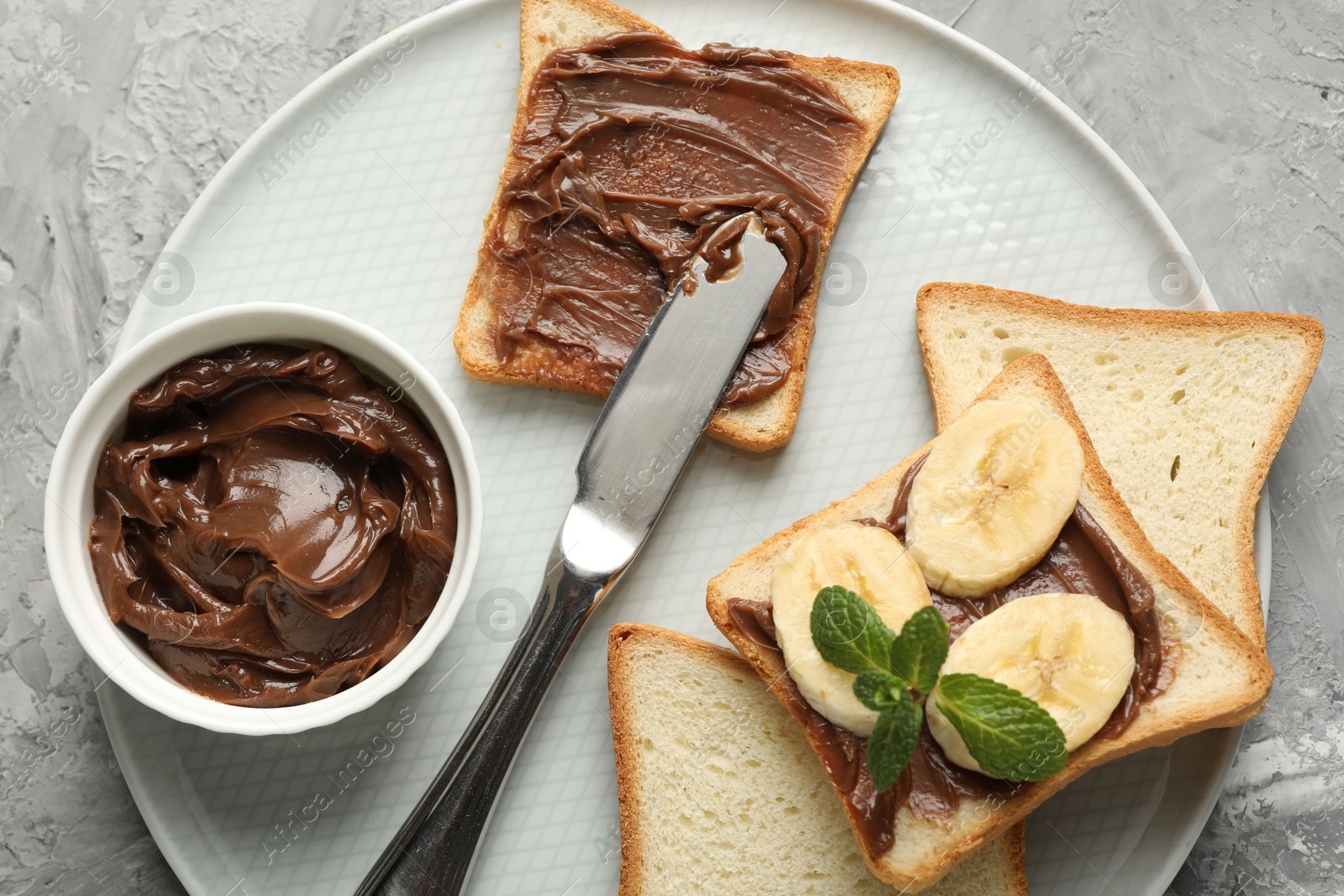 Photo of Sandwiches with chocolate butter, banana, mint and knife on grey table, top view