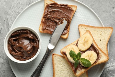 Photo of Sandwiches with chocolate butter, banana, mint and knife on grey table, top view