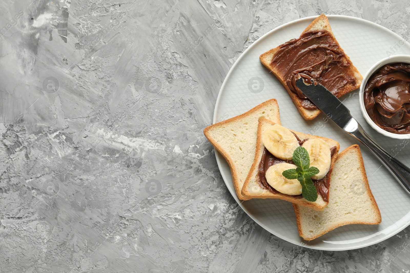 Photo of Sandwiches with chocolate butter, banana, mint and knife on grey table, top view. Space for text