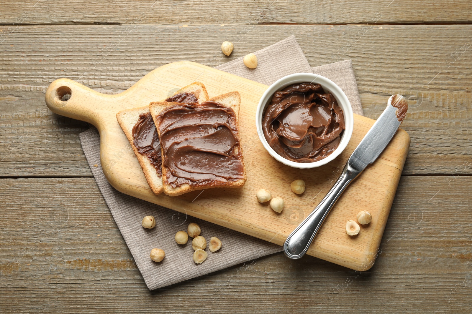 Photo of Sandwiches with chocolate butter, hazelnuts and knife on wooden table, flat lay