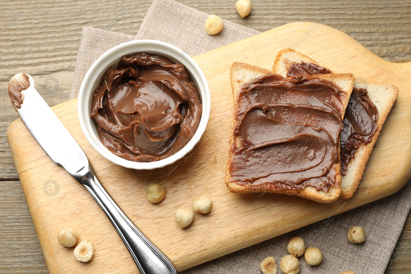 Photo of Sandwiches with chocolate butter, hazelnuts and knife on wooden table, flat lay