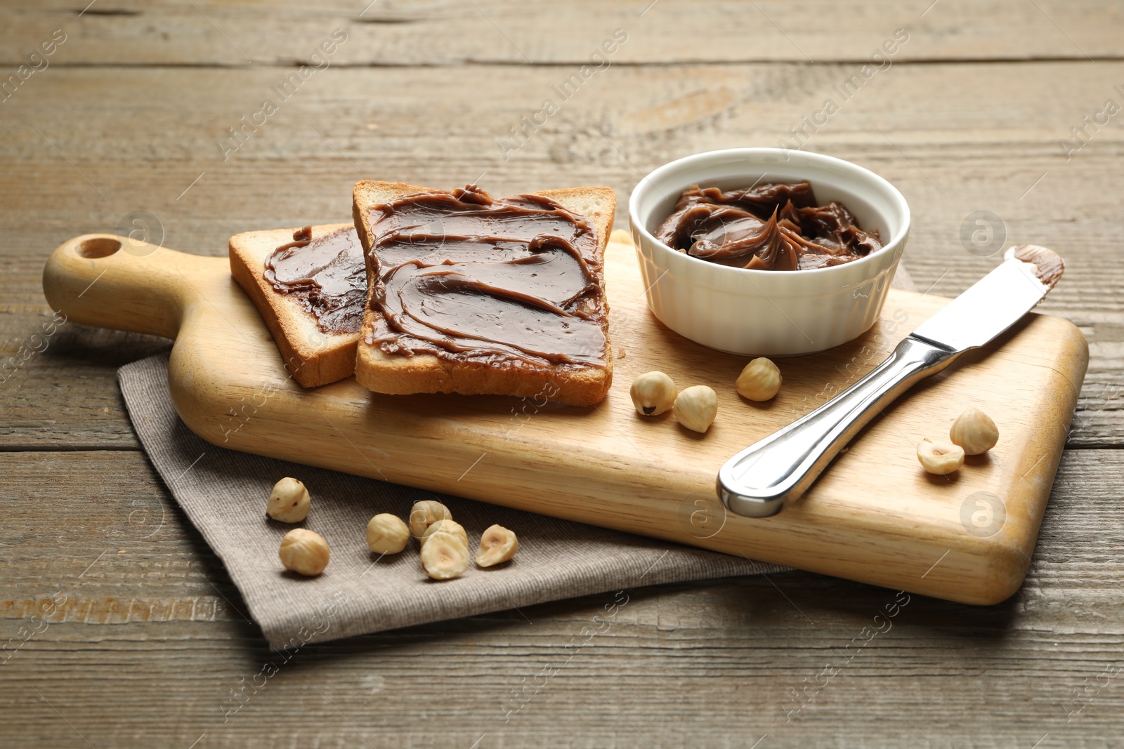 Photo of Sandwiches with chocolate butter, hazelnuts and knife on wooden table, closeup