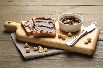 Photo of Sandwiches with chocolate butter, hazelnuts and knife on wooden table, closeup