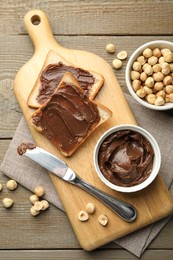 Sandwiches with chocolate butter, hazelnuts and knife on wooden table, flat lay