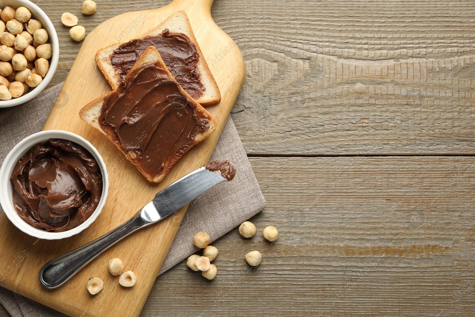 Photo of Sandwiches with chocolate butter, hazelnuts and knife on wooden table, flat lay. Space for text