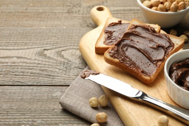 Photo of Sandwiches with chocolate butter, hazelnuts and knife on wooden table, closeup. Space for text