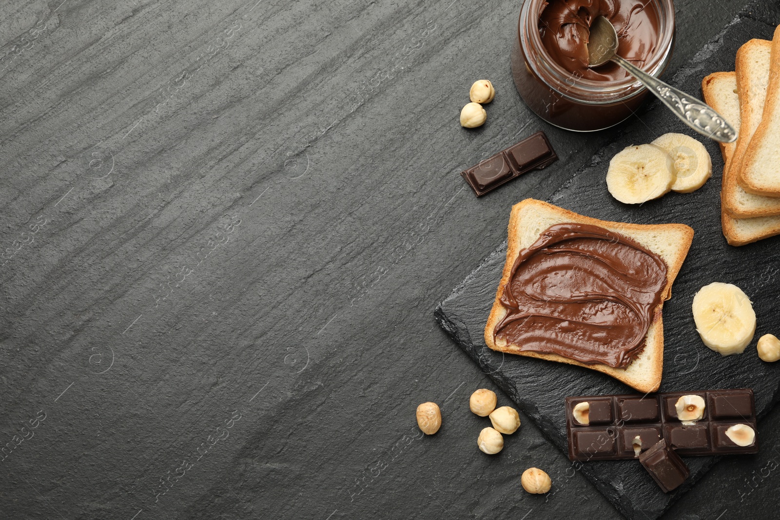 Photo of Sandwich with chocolate butter, banana and hazelnuts on black table, flat lay. Space for text