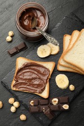 Photo of Sandwich with chocolate butter, banana and hazelnuts on black table, flat lay