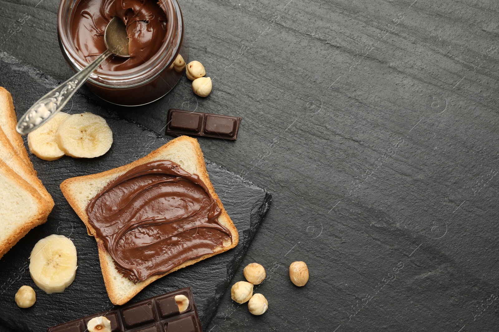 Photo of Sandwich with chocolate butter, banana and hazelnuts on black table, flat lay. Space for text