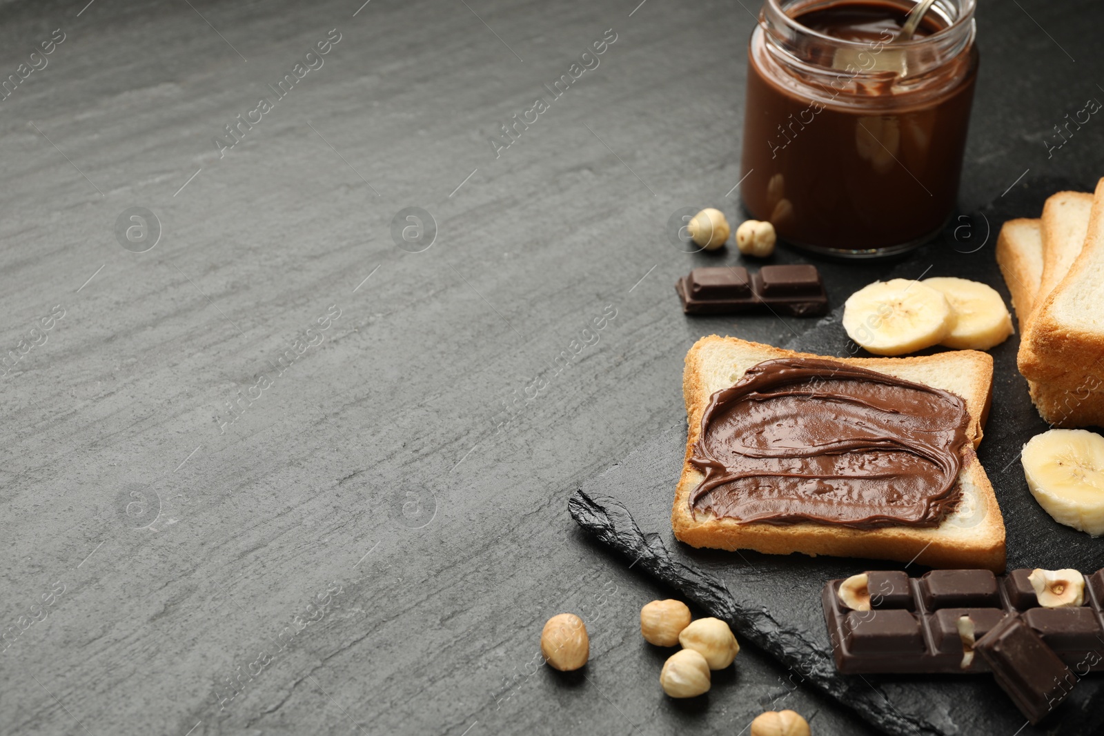 Photo of Sandwich with chocolate butter, banana and hazelnuts on black table, closeup. Space for text