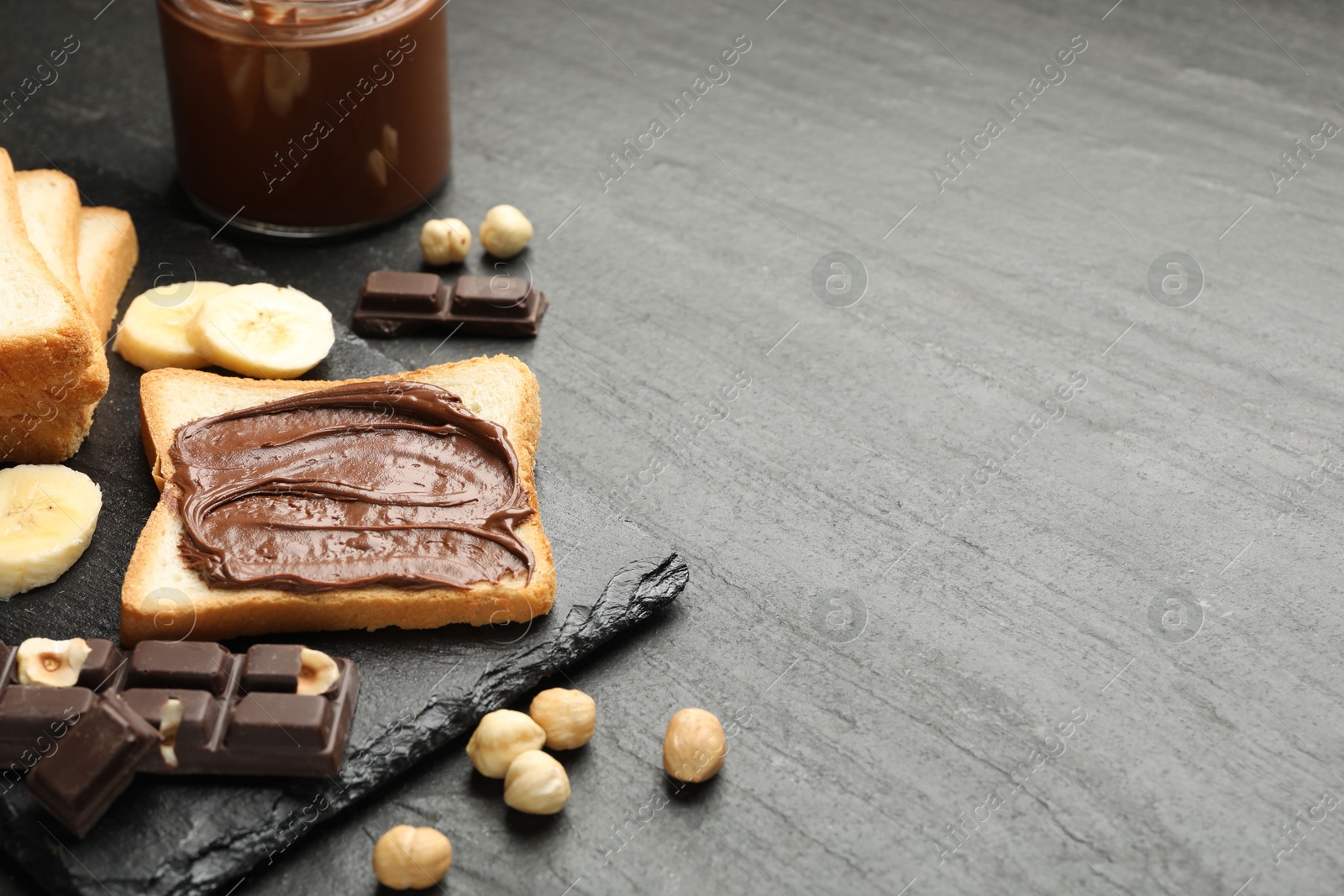 Photo of Sandwich with chocolate butter, banana and hazelnuts on black table, closeup. Space for text