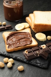 Photo of Sandwich with chocolate butter, banana and hazelnuts on black table, closeup