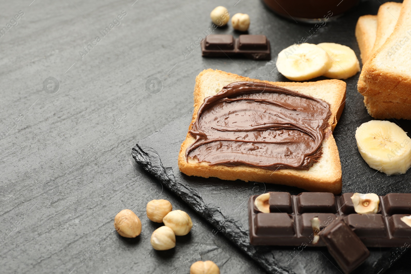 Photo of Sandwich with chocolate butter, banana and hazelnuts on black table, closeup. Space for text