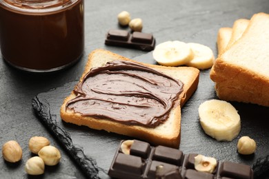 Photo of Sandwich with chocolate butter, banana and hazelnuts on black table, closeup