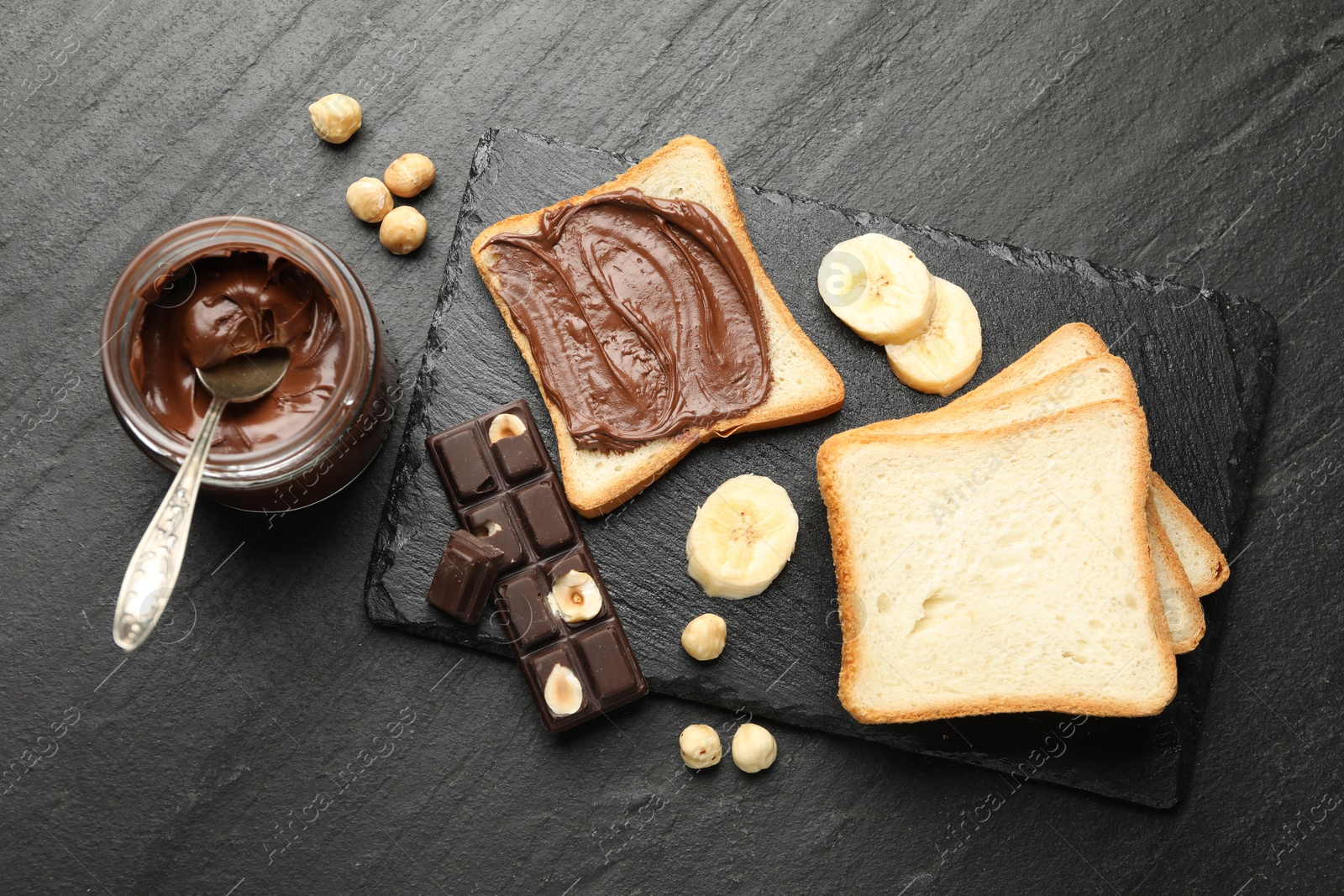 Photo of Sandwich with chocolate butter, banana and hazelnuts on black table, flat lay