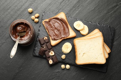 Photo of Sandwich with chocolate butter, banana and hazelnuts on black table, flat lay