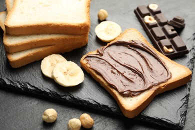 Photo of Sandwich with chocolate butter, banana and hazelnuts on black table, closeup