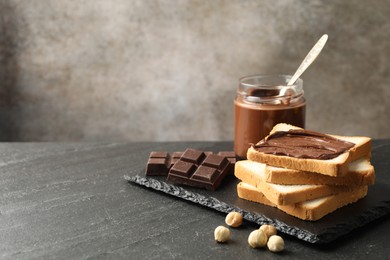 Photo of Sandwich with chocolate butter and hazelnuts on black table, closeup. Space for text