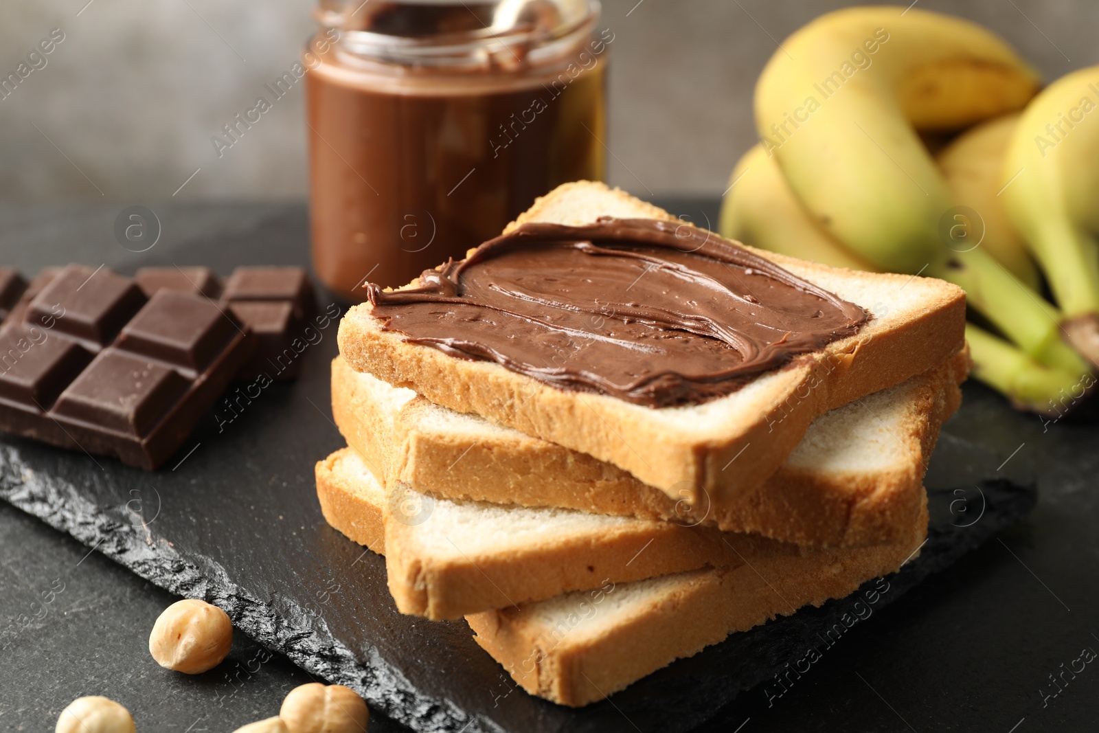 Photo of Sandwich with chocolate butter, hazelnuts and bananas on black table, closeup