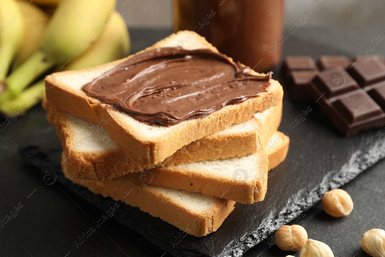 Photo of Sandwich with chocolate butter, hazelnuts and bananas on black table, closeup