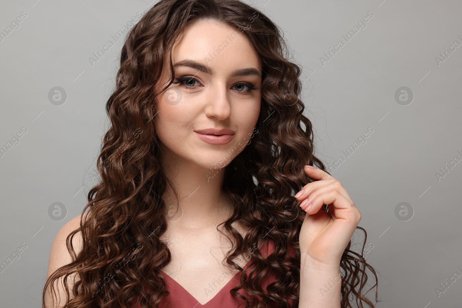 Photo of Beautiful young woman with long curly brown hair on grey background