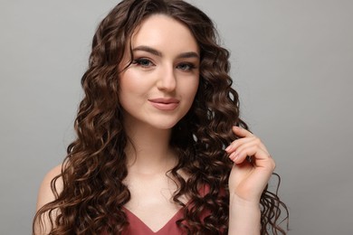 Photo of Beautiful young woman with long curly brown hair on grey background