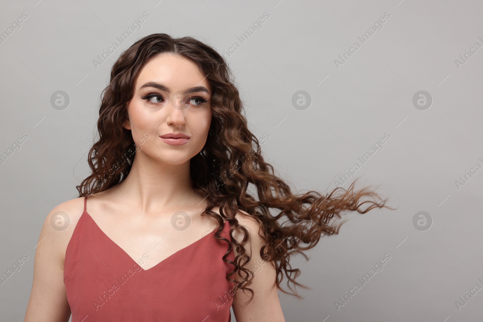 Photo of Beautiful young woman with long curly brown hair on grey background, space for text