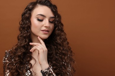 Photo of Beautiful young woman with long curly hair in sequin dress on brown background, space for text