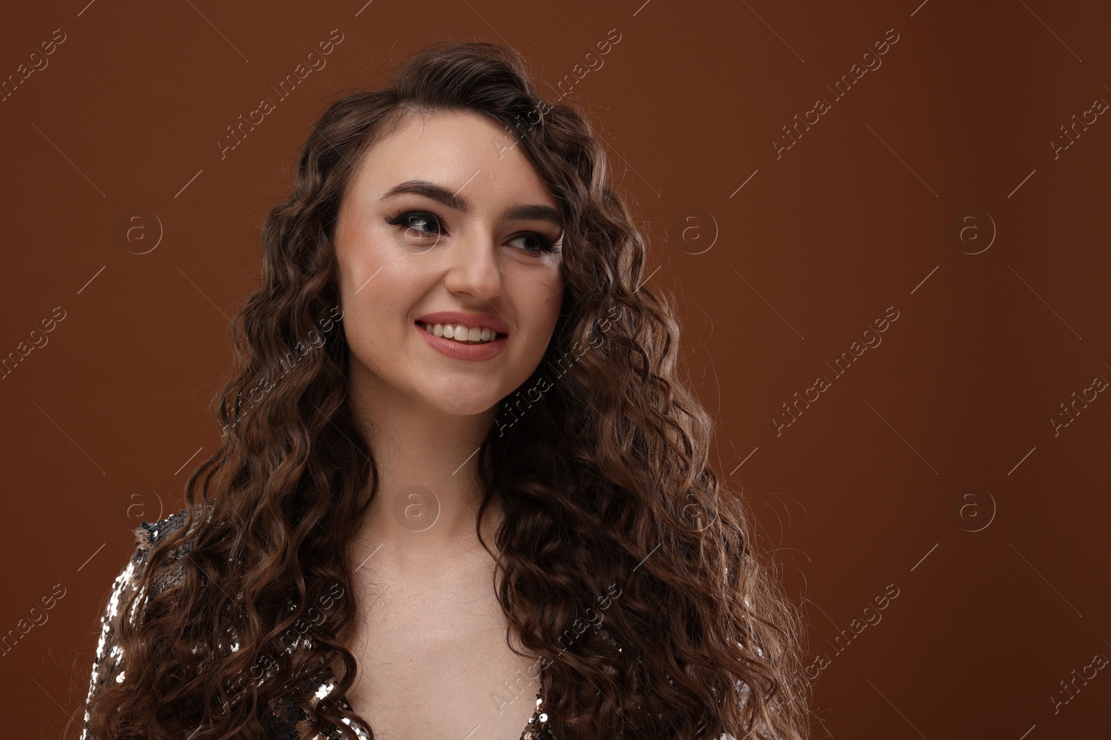 Photo of Beautiful young woman with long curly hair in sequin dress on brown background, space for text