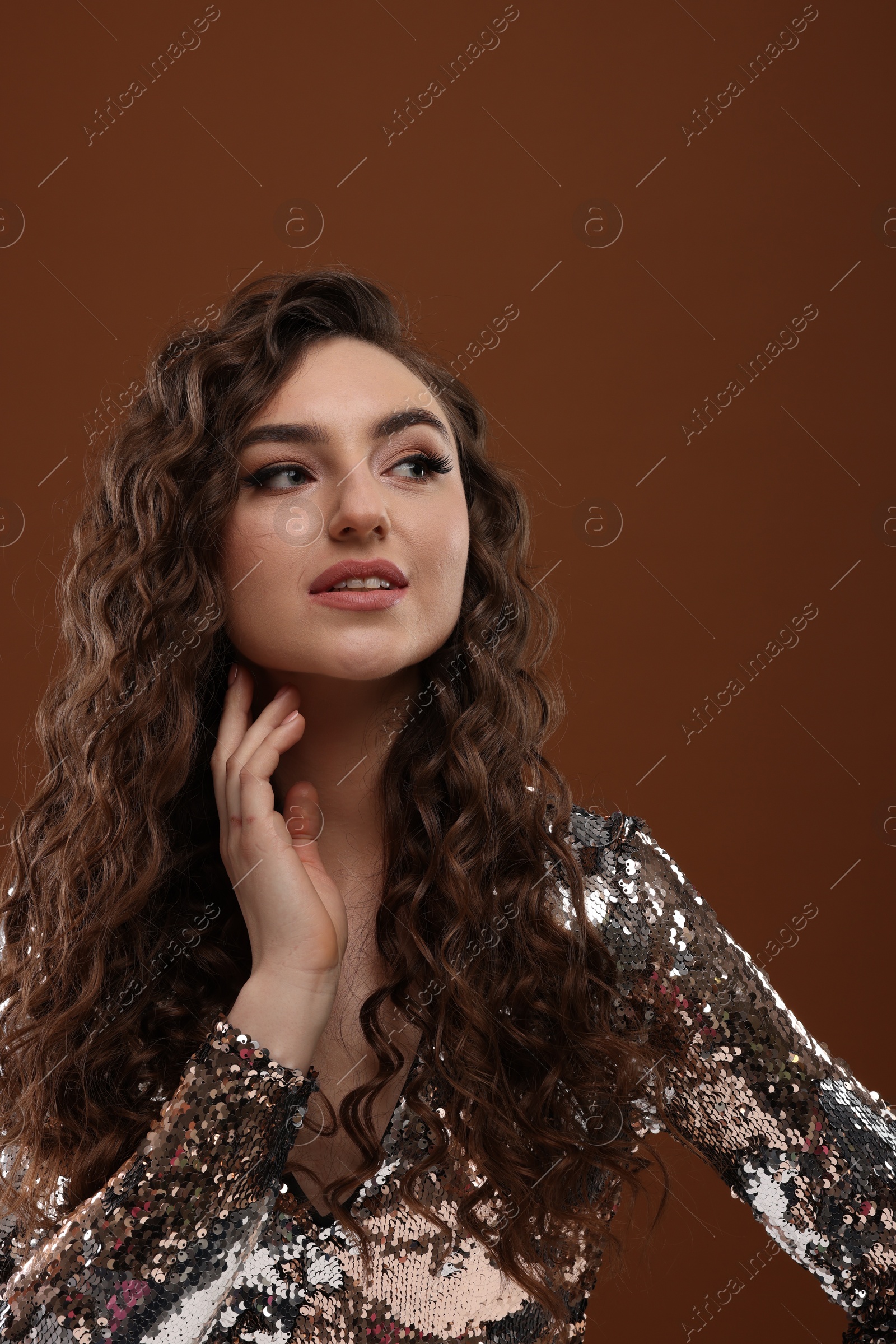 Photo of Beautiful young woman with long curly hair in sequin dress on brown background