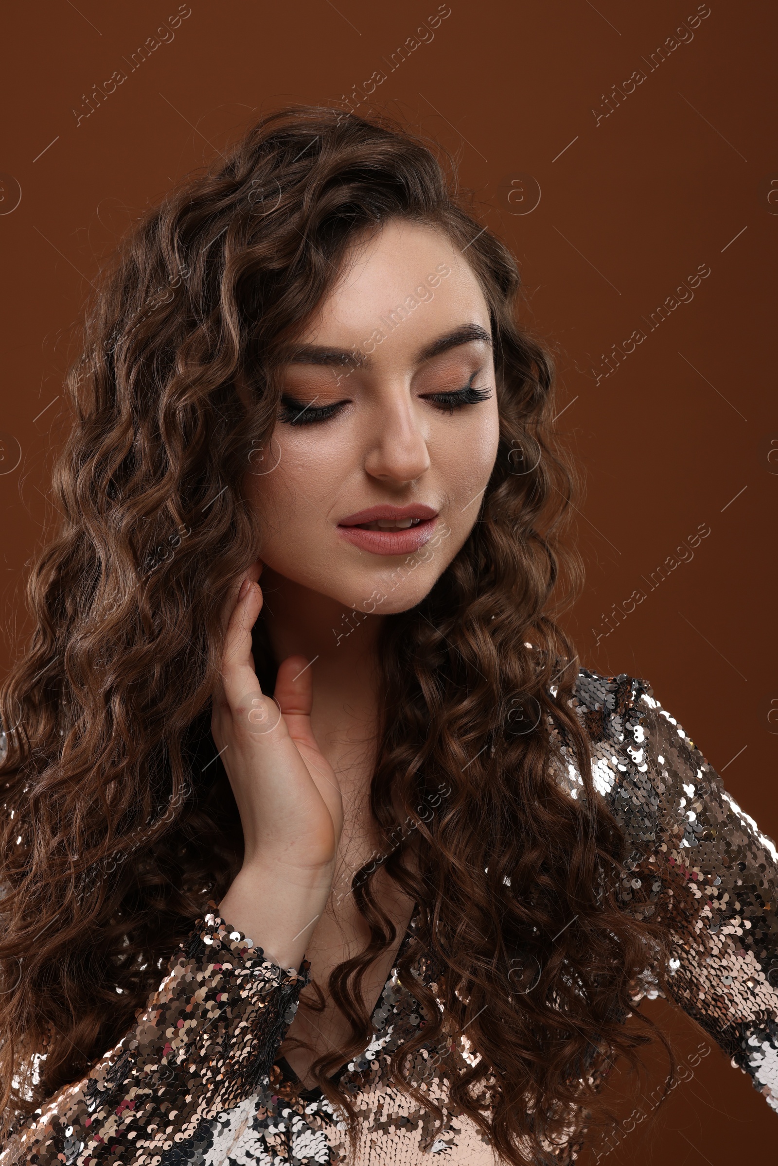 Photo of Beautiful young woman with long curly hair in sequin dress on brown background