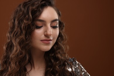 Photo of Beautiful young woman with long curly hair in sequin dress on brown background, closeup. Space for text