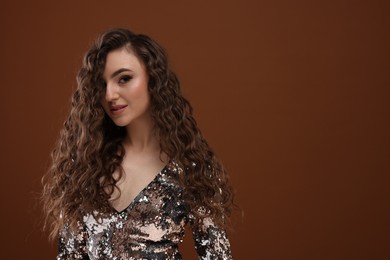 Photo of Beautiful young woman with long curly hair in sequin dress on brown background, space for text