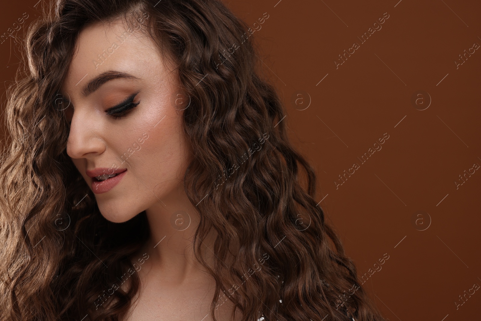 Photo of Beautiful young woman with long curly hair on brown background, closeup. Space for text