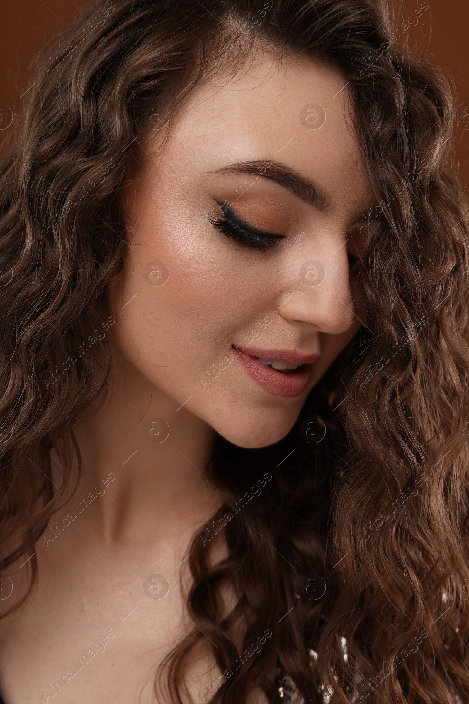 Photo of Beautiful young woman with long curly hair on brown background, closeup