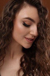 Photo of Beautiful young woman with long curly hair on brown background, closeup