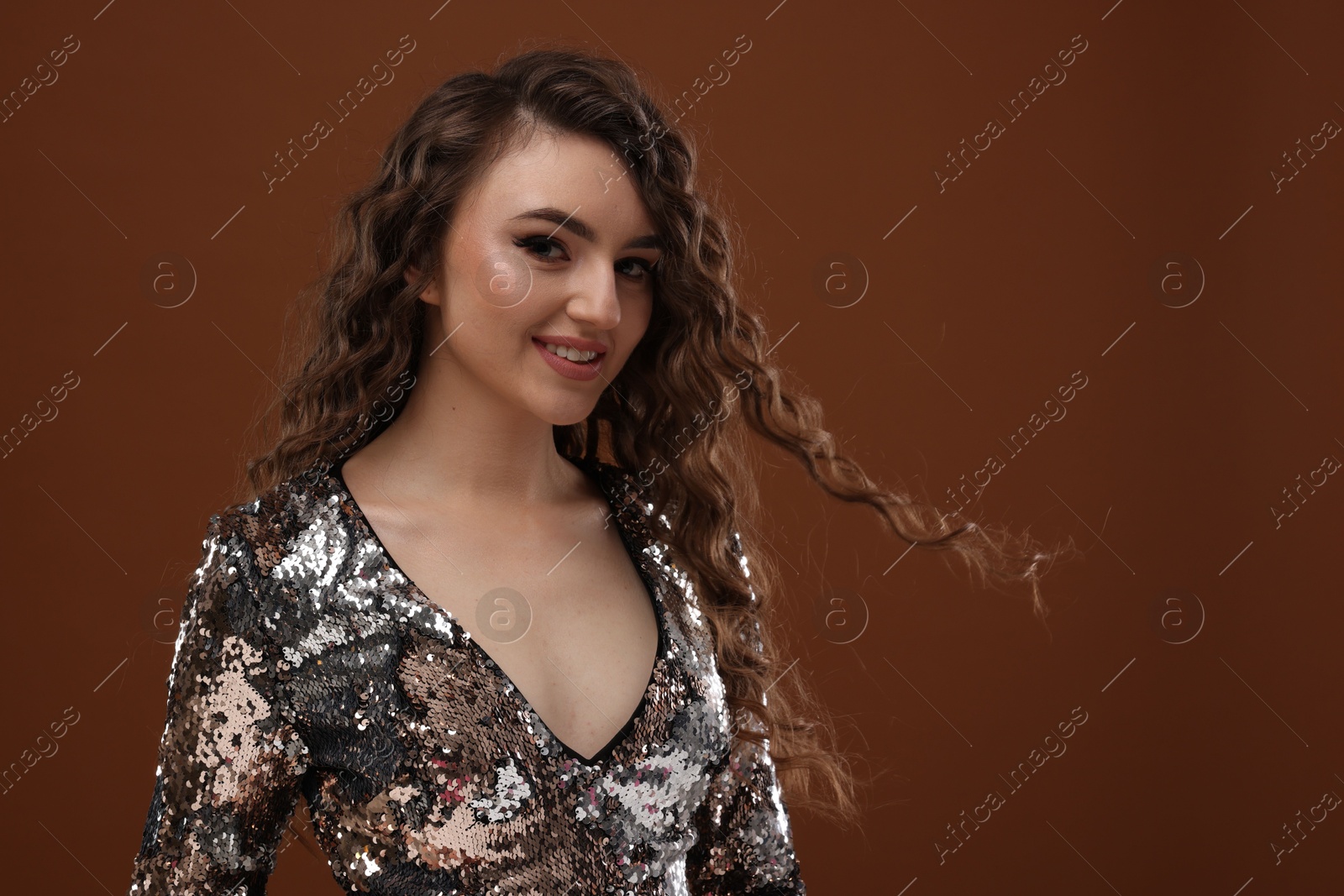 Photo of Beautiful young woman with long curly hair in sequin dress on brown background, space for text