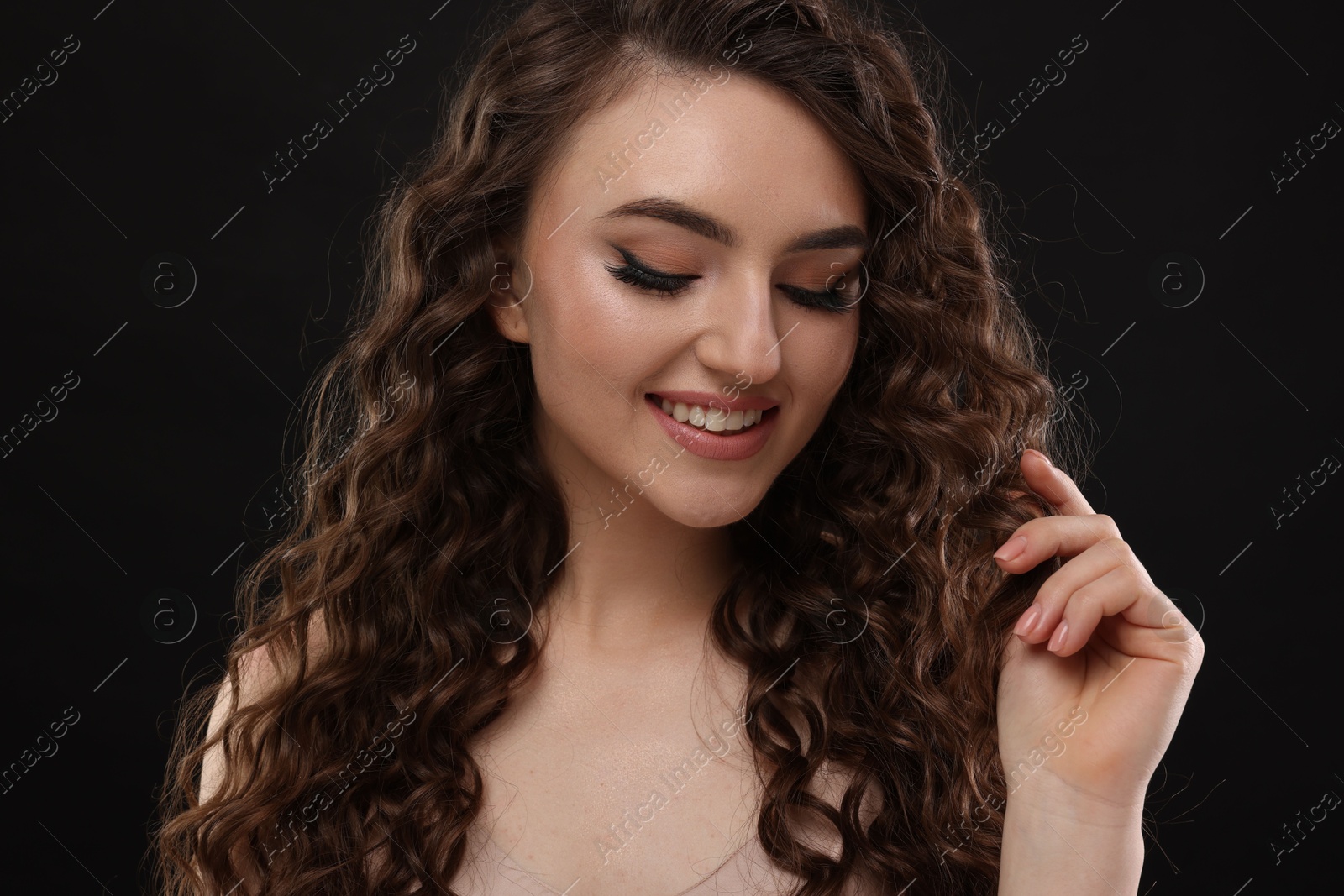 Photo of Beautiful young woman with long curly brown hair on black background