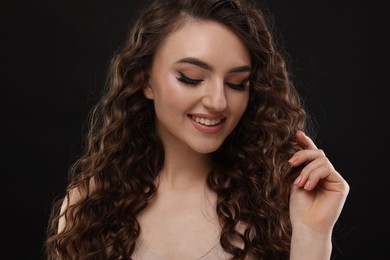 Photo of Beautiful young woman with long curly brown hair on black background