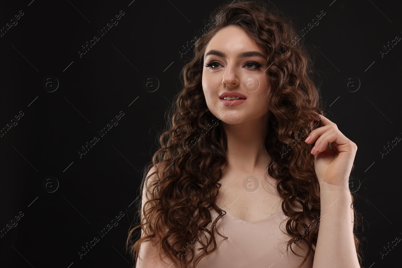 Photo of Beautiful young woman with long curly brown hair on black background, space for text